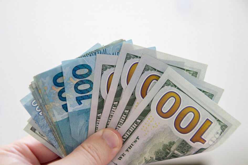 Mão segura notas de US$ 100 e R$ 100