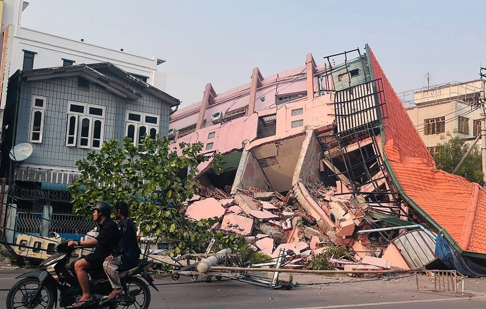 Pessoas passam de moto por um prédio desabado em Mandalay
