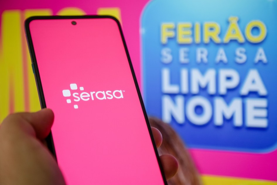 Celular com logo do Serasa ao lado de cartaz do Feirão Limpa Nome