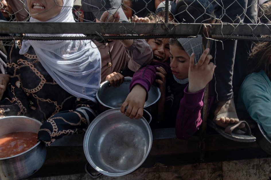 Palestinos deslocados internamente aguardam do lado de fora de uma cozinha comunitária para receber porções limitadas de alimento, em meio à escassez de comida, em Khan Younis, sul da Faixa de Gaza,