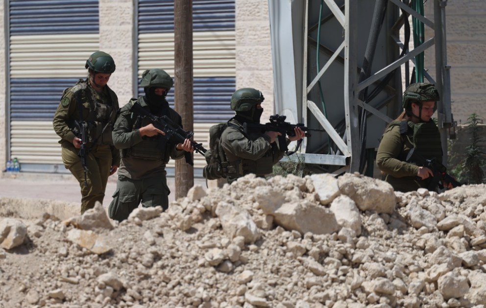 Soldados israelenses fazem guarda enquanto palestinos tentam chegar às suas casas para cuidar de seus pertences no campo de refugiados de Tulkarem