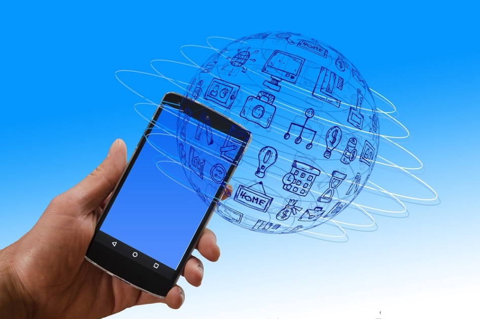 Mão segura um smartphone em um cenário com ym globo e diversos ícones que indicam prosperidade, lazer, finanças e estabilidade econômica