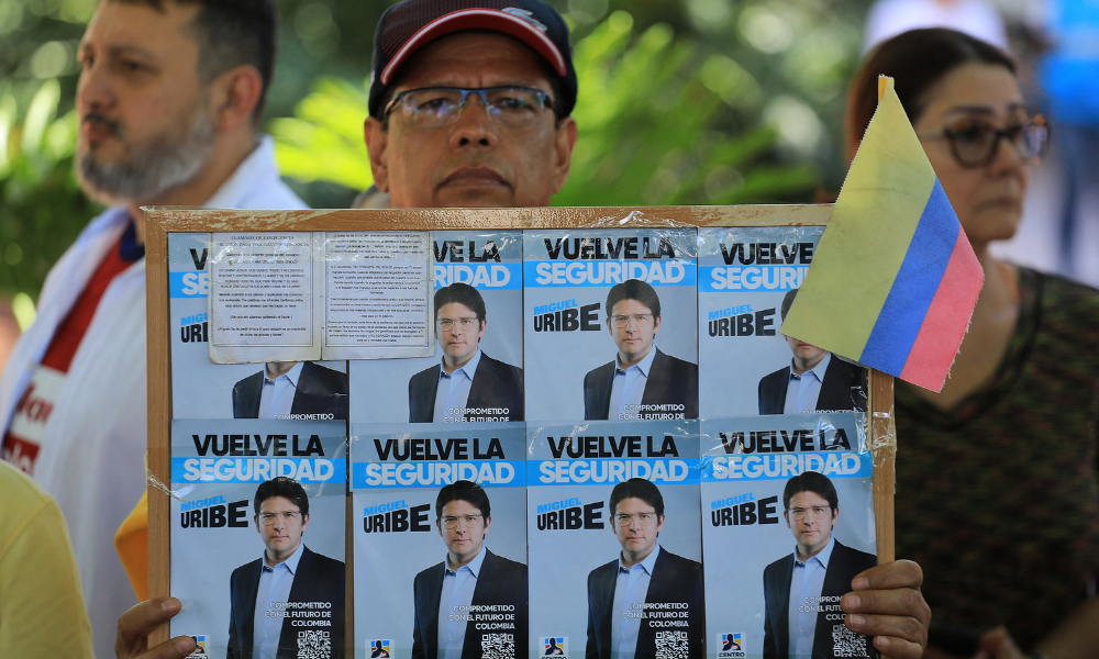 Um homem segura um cartaz com propaganda do candidato à presidência Miguel Uribe durante um protesto contra a violência e em defesa da paz, em Medellín, na Colômbia, em 8 de junho de 2025, um dia após o atentado contra Uribe. Um dos principais candidatos da direita colombiana à presidência, que foi baleado durante um evento de campanha em Bogotá, passou com sucesso por uma cirurgia inicial, informou a prefeita da capital neste domingo. O senador Miguel Uribe, de 39 anos, falava com apoiadores quando um atirador o atingiu com dois tiros na cabeça e um no joelho
