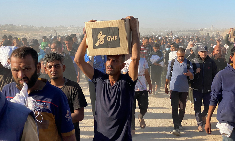 Palestinos deslocados carregam suprimentos de ajuda da Gaza Humanitarian Foundation (GHF), uma organização privada apoiada pelos Estados Unidos que tem contornado o tradicional sistema liderado pela ONU no território, e retornam dos centros de distribuição em Rafah para suas tendas, no sul da Faixa de Gaza, em 29 de maio de 2025. A situação humanitária em Gaza — onde a ajuda começou finalmente a chegar após dois meses de bloqueio — é crítica, após 18 meses de guerra devastadora entre Israel e o movimento palestino Hamas. Especialistas em segurança alimentar alertam que a fome ameaça uma em cada cinco pessoas. (Foto: AFP)