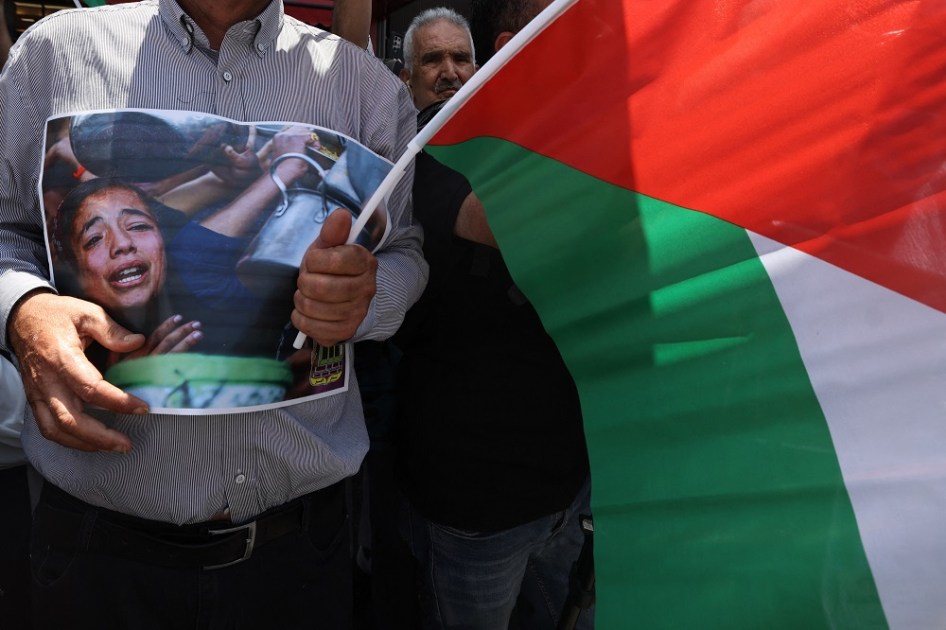 Um palestino carrega um cartaz e agita a bandeira nacional durante uma manifestação em apoio aos palestinos na Faixa de Gaza, que enfrentam grave escassez de alimentos e outros itens essenciais, na cidade de Nablus, na Cisjordânia ocupada por Israel