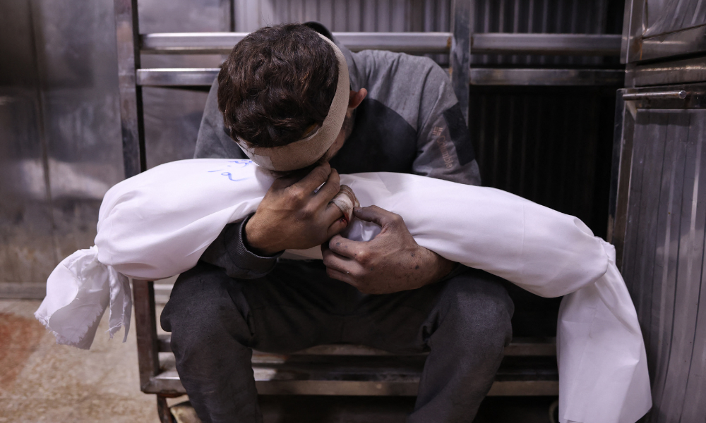 Conteúdo gráfico / Um homem palestino chora enquanto segura o corpo envolto em manto de uma criança, morta em ataques israelenses durante a noite, no necrotério do hospital Al-Shifa, na Cidade de Gaza, em 15 de julho de 2025. (Foto de Omar AL-QATTAA / AFP)