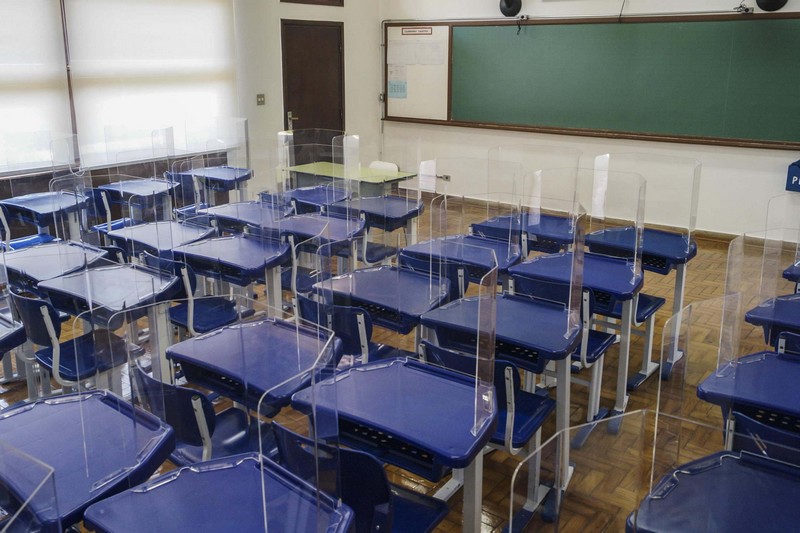 sala de aula vazia com equipamento de proteção nas carteiras para garantir o distanciamento dos alunos
