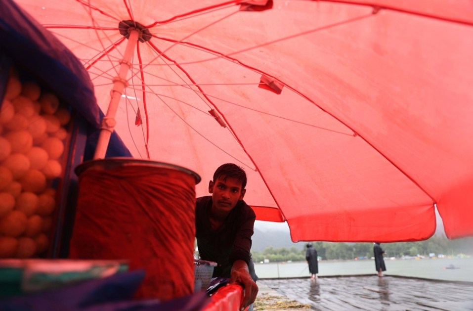 Vendedor ambulante se abriga sob o guarda-chuva de sua carroça durante a chuva em Srinagar, Índia
