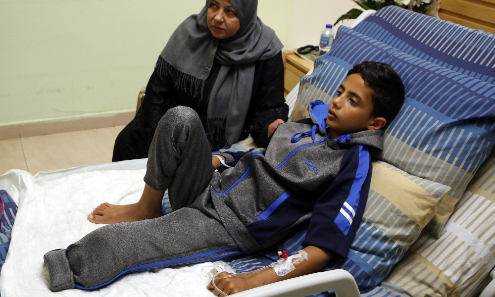 Abdel Rahman Nawfal, de 12 anos, senta-se ao lado da avó em um hospital na cidade de Ramallah, na Cisjordânia, em 23 de abril de 2018, após ter sua perna amputada devido a um ferimento sofrido durante confrontos com forças israelenses perto da fronteira entre Gaza e Israel. (Foto de ABBAS MOMANI / AFP)