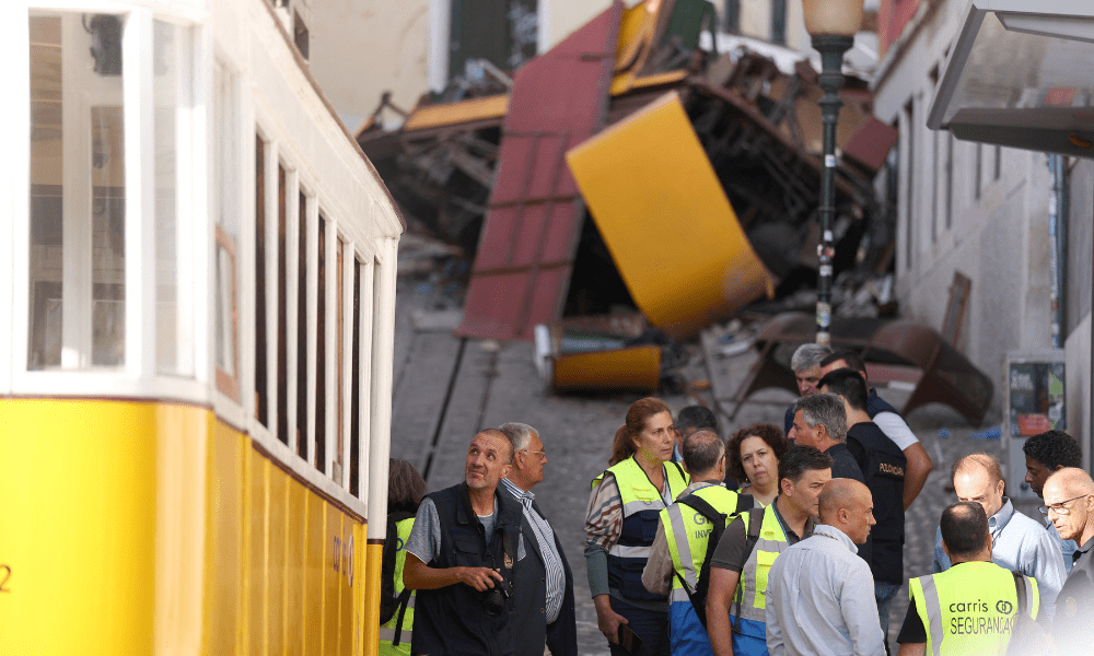 Investigadores da polícia (E) são fotografados ao lado de funcionários da empresa de transportes La Carris, de Lisboa, com os destroços do funicular da Glória ao fundo, um dia após o acidente que matou 15 pessoas em Lisboa, em 4 de setembro de 2025. Pelo menos 15 pessoas morreram e outras 18 ficaram feridas quando um famoso funicular descarrilou em Lisboa em 3 de setembro de 2025, segundo equipes de resgate. (Foto de PATRICIA DE MELO MOREIRA / AFP)
