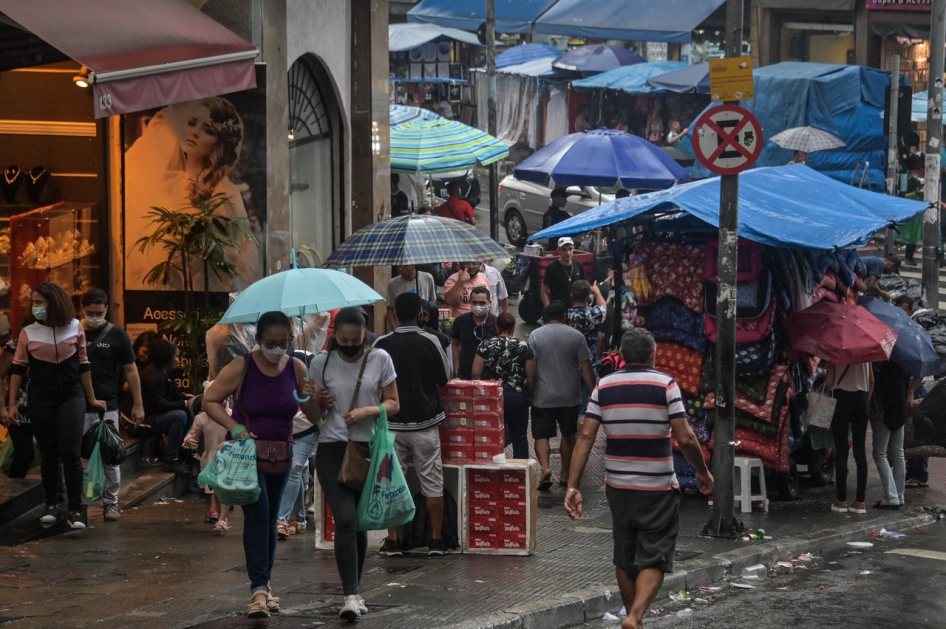 Pessoas caminham em rua de comércio com bolsas nas mãos