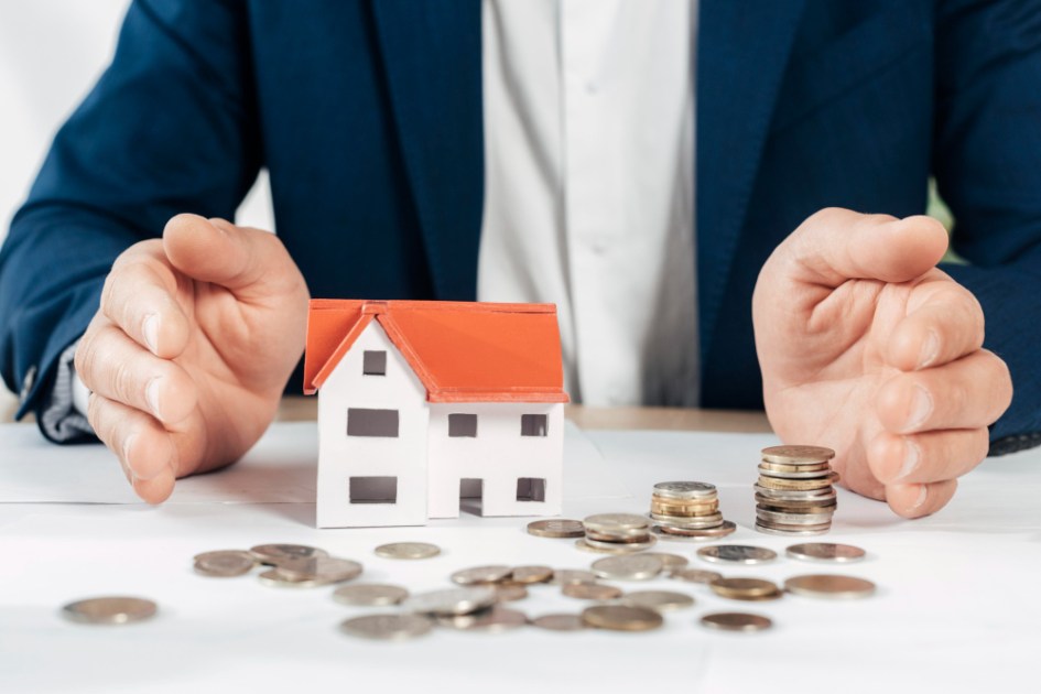 Homem em mesa com maquete de casa e moedas