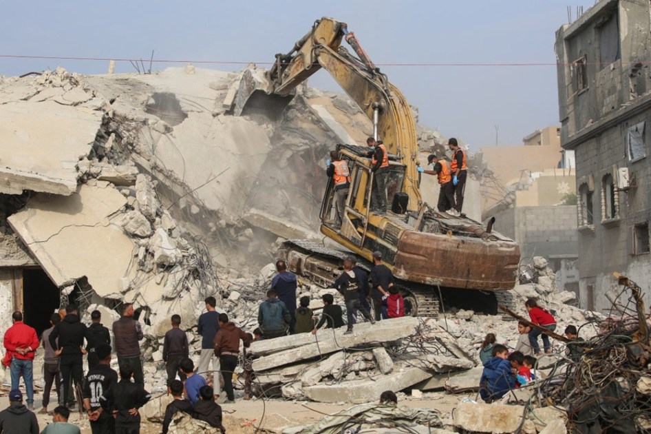 Integrantes da Defesa Civil usam uma escavadeira para procurar os restos de vítimas nos escombros de um prédio destruído no campo de refugiados de Bureij, no centro da Faixa de Gaza