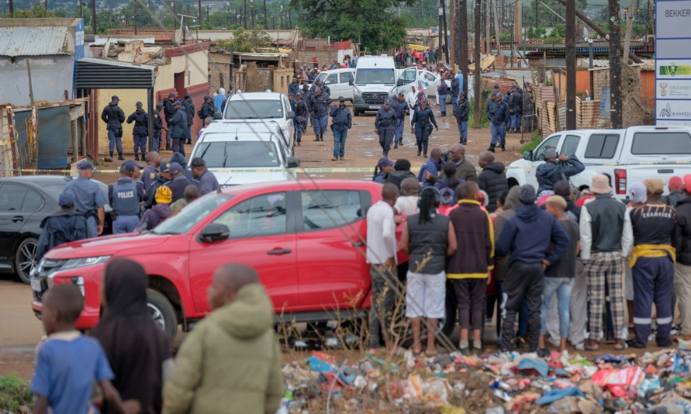 Moradores observam enquanto policiais do Serviço de Polícia Sul-Africano (SAPS) se reúnem no local do ataque a um bar, em Bekkersdal