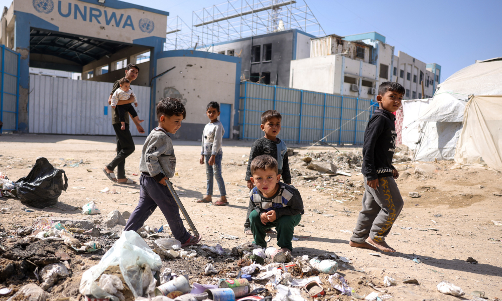 Crianças brincam perto do lixo em frente à sede fechada da agência da ONU para refugiados palestinos (UNRWA), na Cidade de Gaza, em 20 de maio de 2025, em meio à guerra em curso entre Israel e o movimento militante palestino Hamas. Israel, impulsionando uma ofensiva militar recentemente expandida na Faixa de Gaza, tem enfrentado crescente pressão, inclusive de um dos principais apoiadores, os Estados Unidos, para pôr fim ao bloqueio de ajuda humanitária imposto em 2 de março. (Foto de Bashar TALEB / AFP)