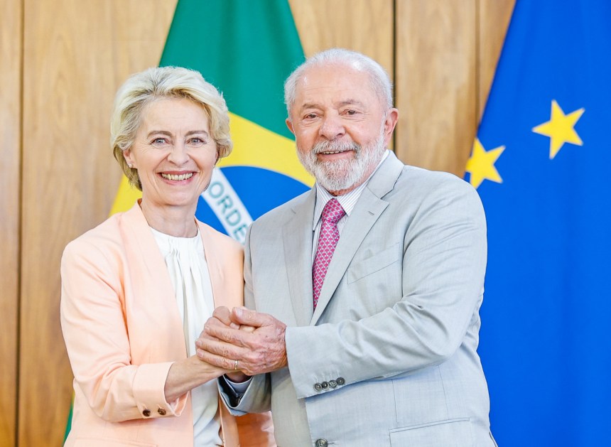 Ursula Von der Leyn e Lula posam com as mãos entrelaçadas; atrás, as bandeiras do Brasil e da União Europeia