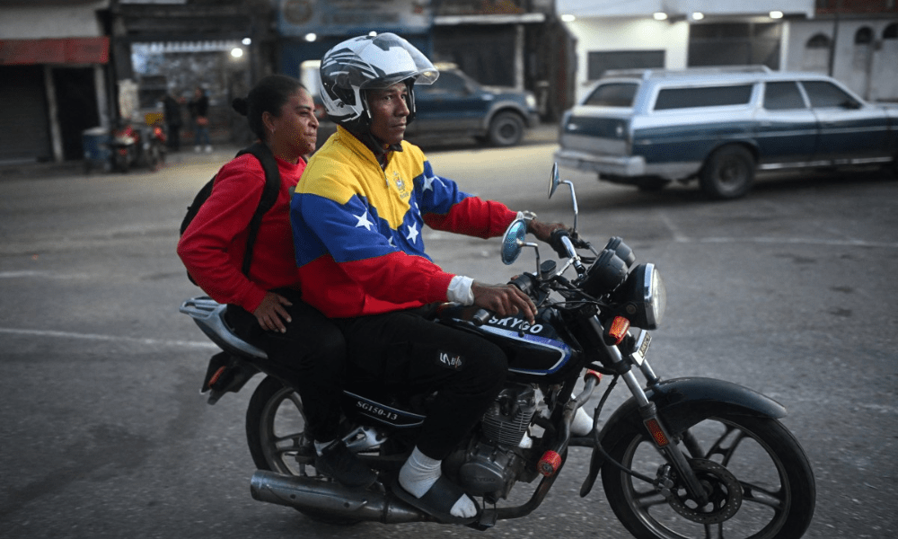 Mototaxista vestindo uma jaqueta com a bandeira da Venezuela transporta um passageiro nos arredores da prisão El Rodeo I em Guatire, estado de Miranda, a cerca de 30 quilômetros a leste de Caracas