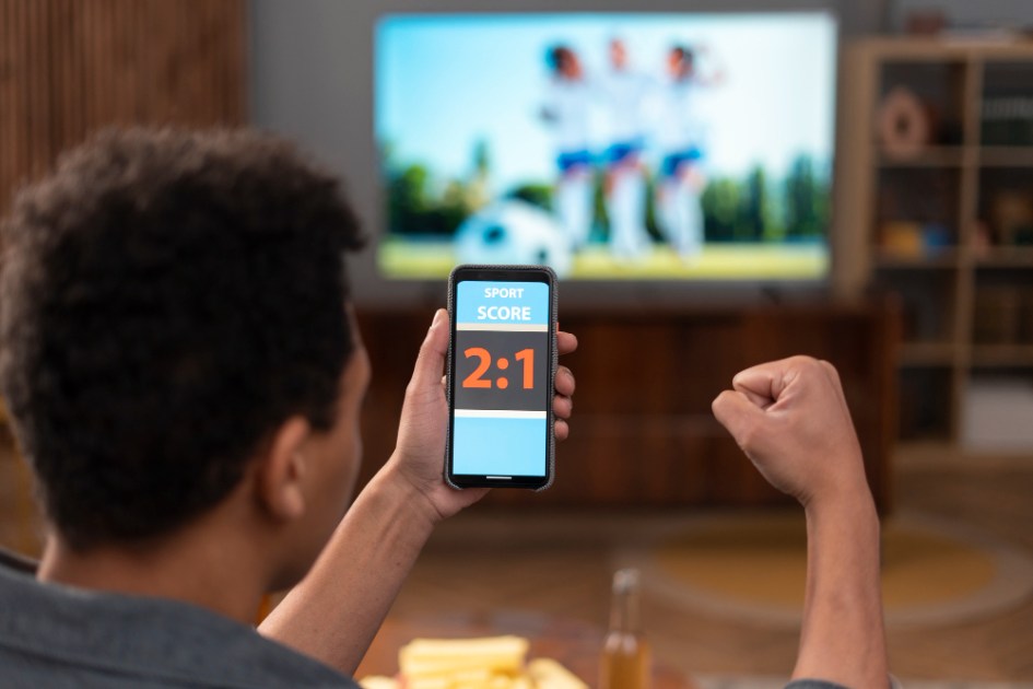 Homem segura celular segurando placar e vibra com gol na TV