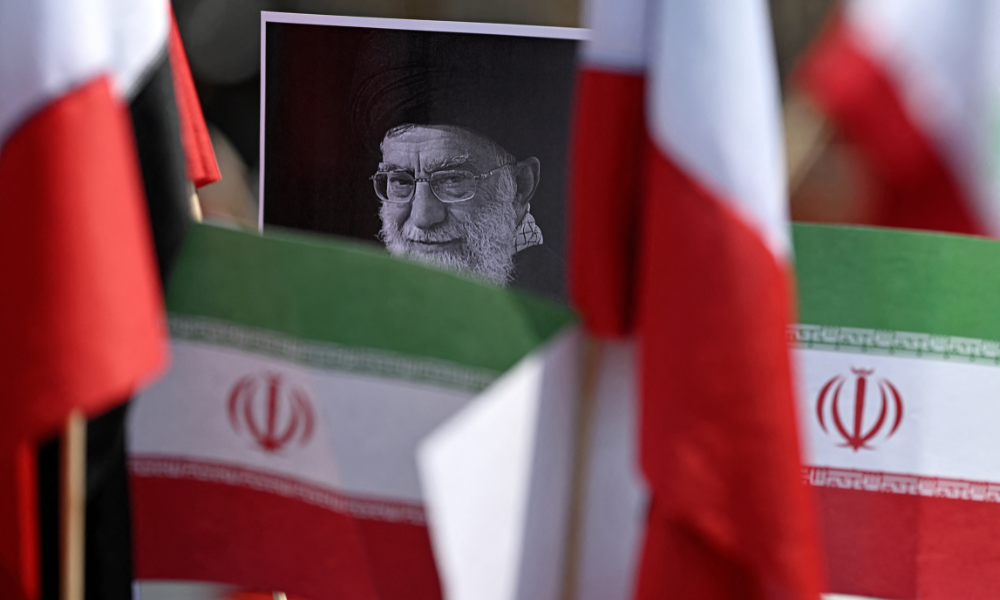 Um manifestante segura um cartaz com a imagem do falecido Líder Supremo iraniano, Aiatolá Ali Khamenei, cercado por bandeiras iranianas, em frente ao consulado dos EUA, durante um protesto contra o conflito no Oriente Médio, na Cidade do México, em 7 de março de 2026. (Foto de Carl de Souza / AFP)