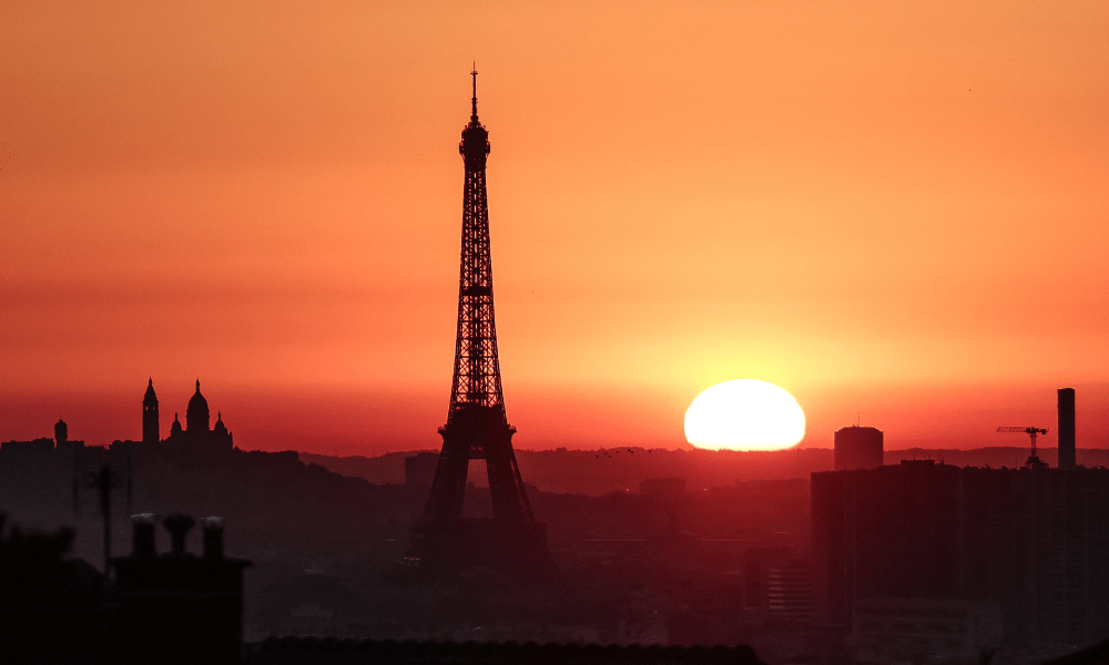 O sol nasce perto da Torre Eiffel e da Basílica do Sagrado Coração, no topo da colina de Montmartre, em Paris, em 1º de julho de 2025, enquanto a cidade está em alerta vermelho para altas temperaturas, com o topo da Torre Eiffel fechado, o trânsito poluente proibido e restrições de velocidade em vigor, enquanto uma onda de calor escaldante atinge a Europa. As mudanças climáticas causadas pelo homem tornaram a recente onda de calor europeia até 4°C mais quente em muitas cidades, disseram cientistas em 9 de julho de 2025, elevando as temperaturas a um nível mortal para milhares de pessoas vulneráveis. (Foto de Thibaud MORITZ / AFP)