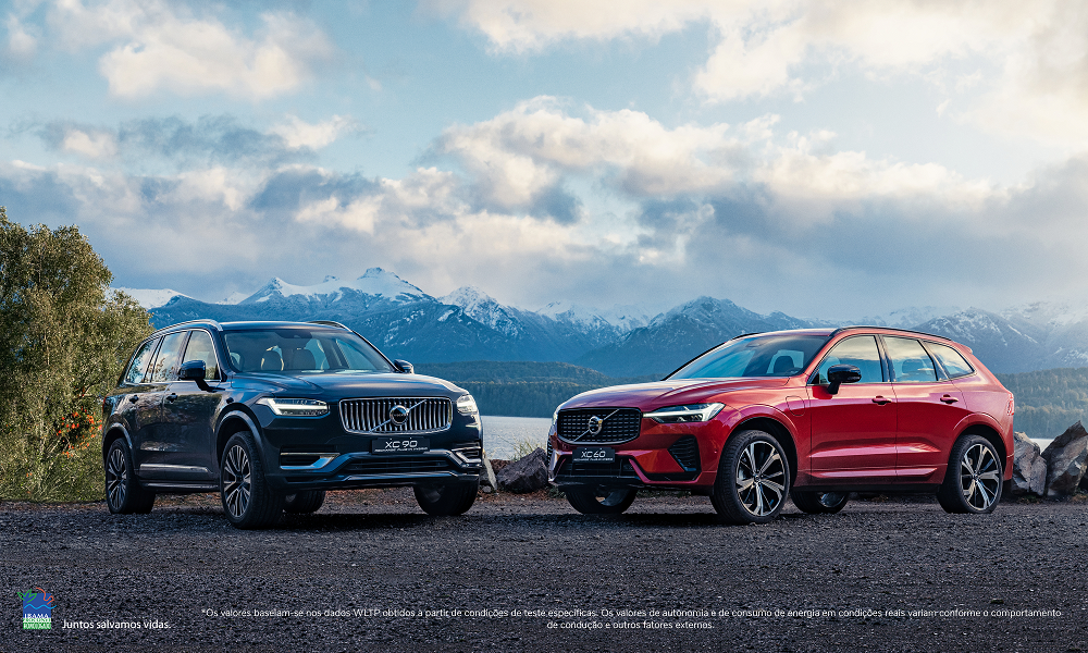 Dois carros da Volvo, um chumbo e outro vermelho, parados em uma estrada, de costas para a montanha