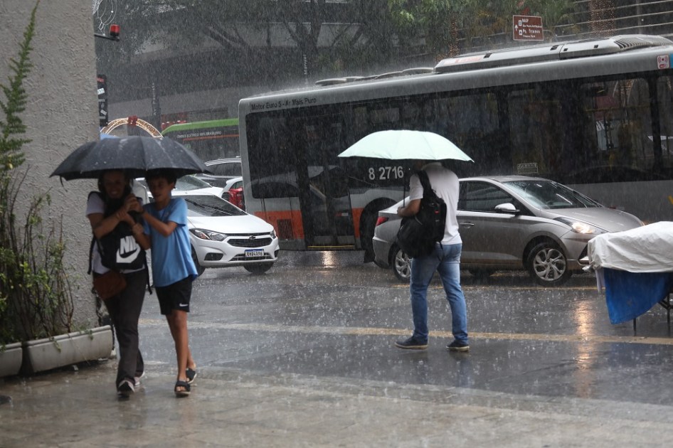 Pedestres se protegem da chuva que cai pela Avenida Paulista