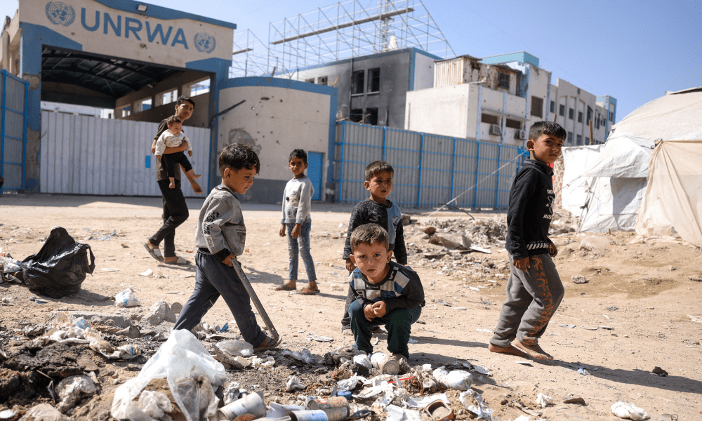 Crianças brincam em meio ao lixo em frente à sede fechada da UNRWA, a agência da ONU para refugiados palestinos, na Cidade de Gaza, em 20 de maio de 2025, em meio à guerra em curso entre Israel e o movimento militante palestino Hamas. Israel, intensificando sua ofensiva militar na Faixa de Gaza, enfrenta crescente pressão, inclusive dos Estados Unidos, seu principal aliado, para encerrar o bloqueio à ajuda humanitária imposto em 2 de março. (Foto de Bashar Taleb / AFP)