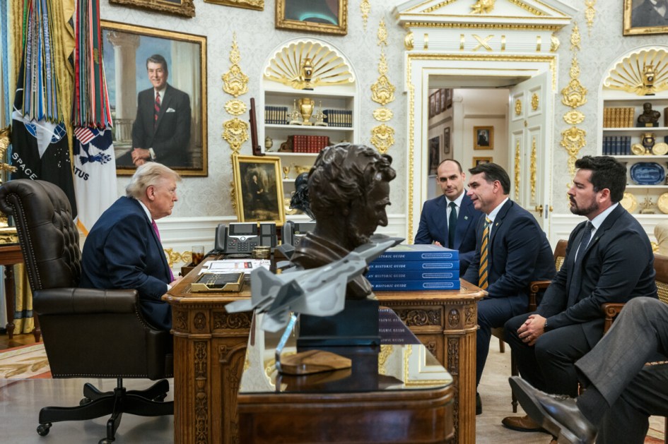 Irmãos Bolsonaro sentados à mesa do Salão Oval com Donald Trump.