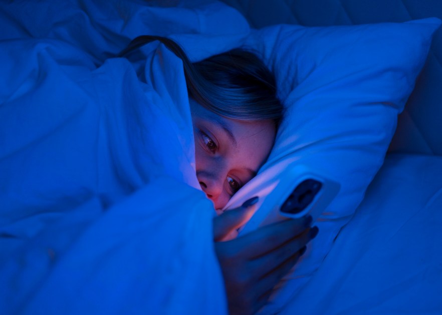 Mulher mexe no celular na cama