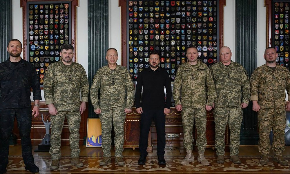 Nesta fotografia divulgada pelo Serviço de Imprensa da Presidência da Ucrânia em 22 de julho de 2026, o Presidente da Ucrânia, Volodymyr Zelensky (C), posa para uma fotografia com o Ministro da Defesa interino da Ucrânia, Yevgeniy Khmara (E), o antigo Chefe do Estado-Maior das Forças Armadas da Ucrânia, Andriy Gnatov (2º E), o antigo Comandante-em-Chefe das Forças Armadas da Ucrânia, Oleksandr Syrsky (3º E), o Comandante-em-Chefe das Forças Armadas da Ucrânia, Mykhailo Drapaty (3º D), o recém-nomeado Chefe do Estado-Maior das Forças Armadas da Ucrânia, Ihor Skybiuk (2º D) e o Vice-Chefe do Gabinete da Presidência da Ucrânia, Pavlo Palisa (D), em Kiev. O líder ucraniano Volodymyr Zelensky anunciou Mykhailo Drapaty como o novo comandante-em-chefe do país, após uma crise política desencadeada pela demissão surpresa, por Zelensky, de um jovem ministro da Defesa defensor da modernização do país.